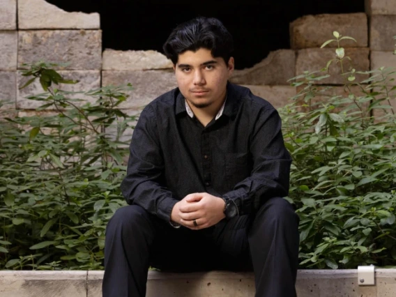 Marcelino Perez seated, wearing all black, on a concrete wall.