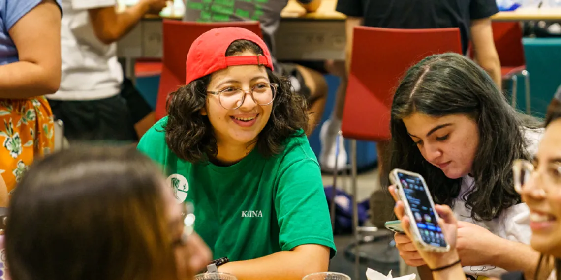 Students sitting at a table. Main studnet is looking off toward the camera and smiling.