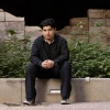 Marcelino Perez seated, wearing all black, on a concrete wall.